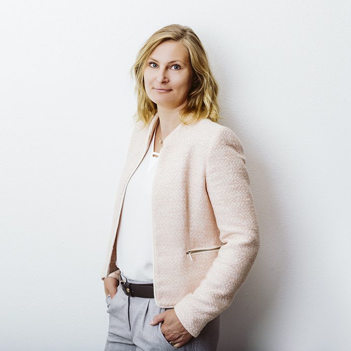 Foto Catrin Strüh-Flament Eine blonde Frau in einem hellen Blazer steht entspannt vor einer weißen Wand.